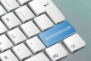 Le clavier d'ordinateur se présente en une teinte blanche, mais la touche Shift se démarque en bleu. Sur cette touche, on peut lire en lettres majuscules l'inscription "MEAN TIME BETWEEN FAILURES".
