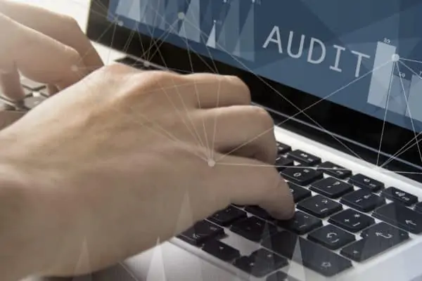 main qui tape sur le clavier d'un ordinateur où sur l'écran il y a écrit Audit